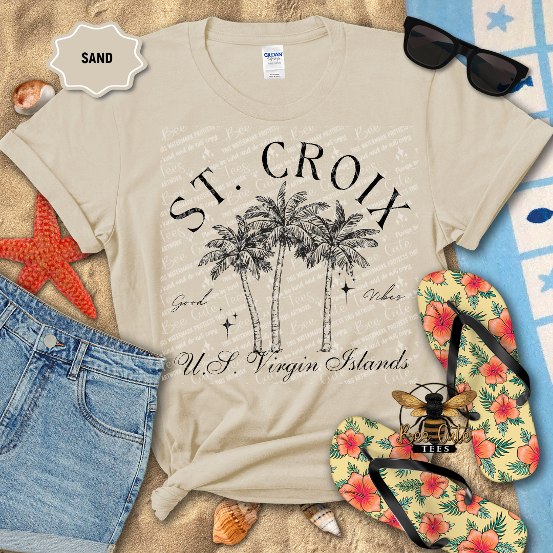 Beige t-shirt with 'St. Croix U.S. Virgin Islands' design on a sandy background with flip-flops and sunglasses.