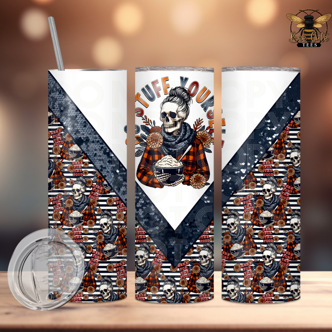 Three tall skinny tumblers with a Halloween-themed wrap design, displayed on a wooden surface with a clear lid and straw in the foreground. The design features a central skull illustration with the text 'STUFF YOURSELF' and patterned sections with skulls, ghosts, and plaid.