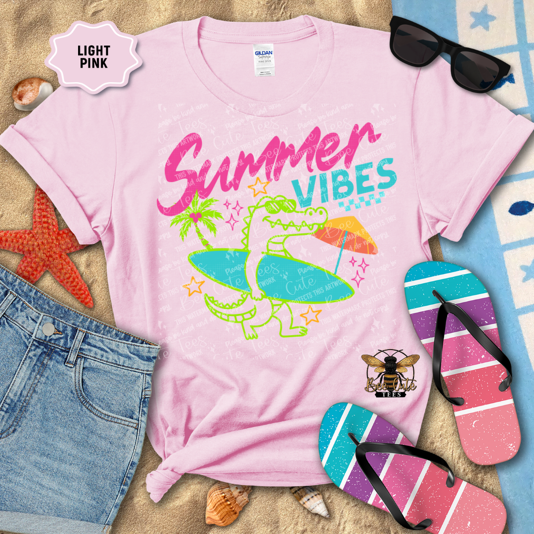 Light pink t-shirt with 'Summer Vibes' design on a sandy background with beach accessories.