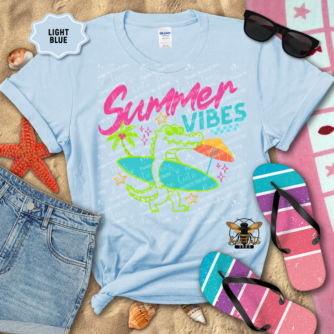 Light blue t-shirt with 'Summer Vibes' graphic on a sandy background with beach accessories.