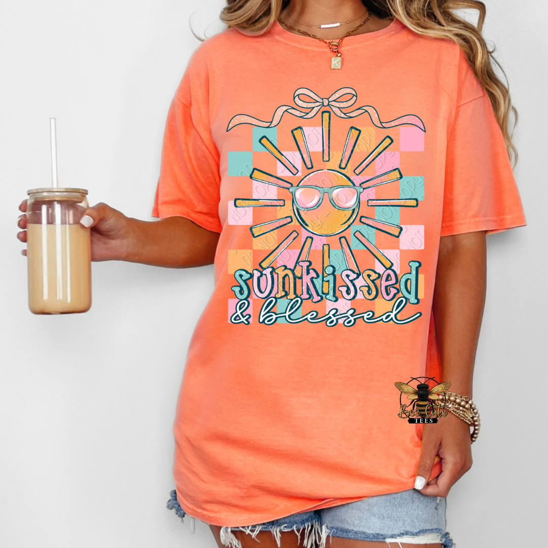 Person wearing an orange t-shirt with a sun graphic and 'funkissed & blessed' text, holding a drink.