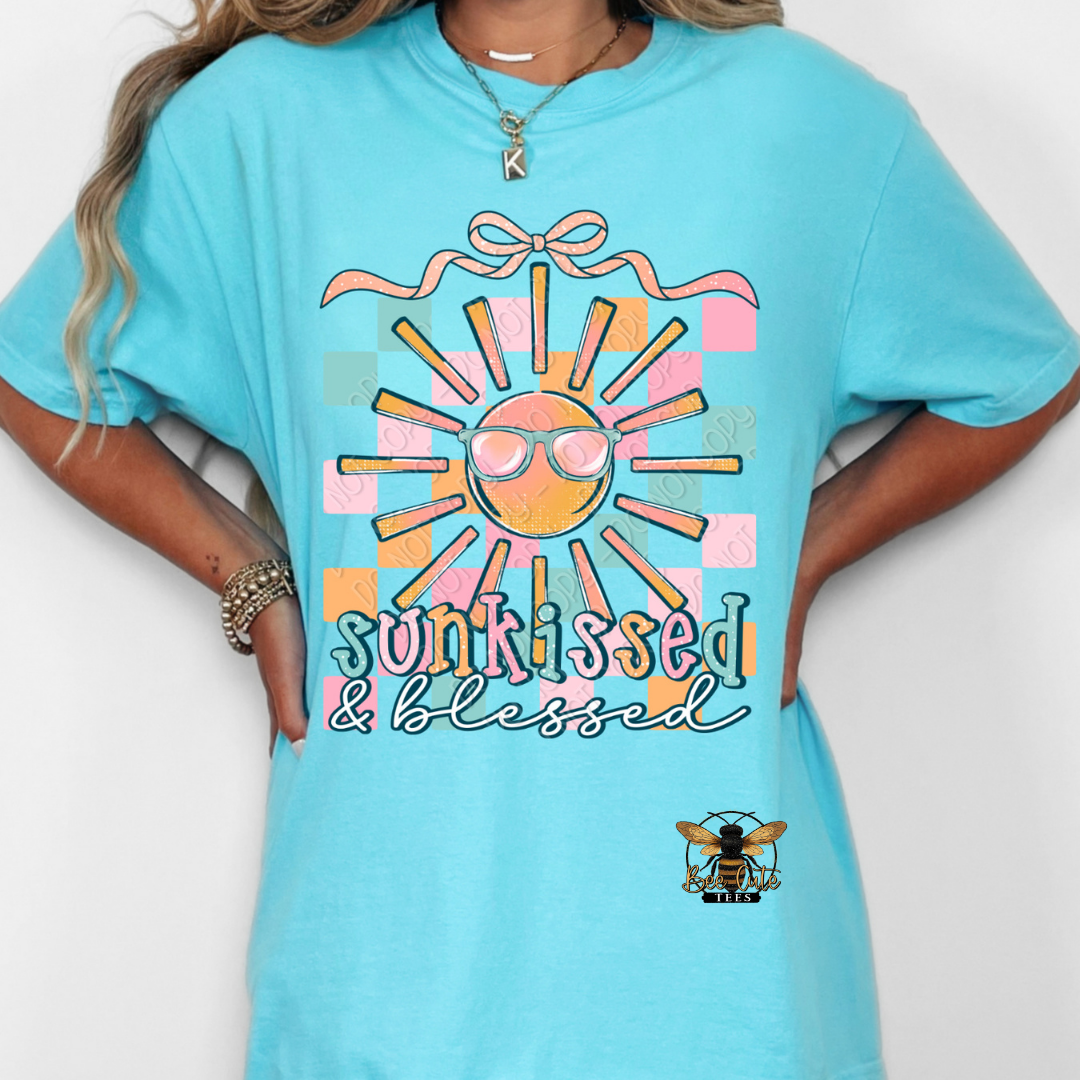 Person wearing a turquoise t-shirt with a colorful sun graphic and 'sunkissed & blessed' text on a white background.