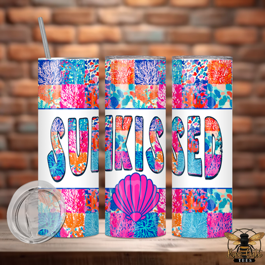 Colorful tumbler with 'Sunkissed' design on a wooden surface with a brick wall background.