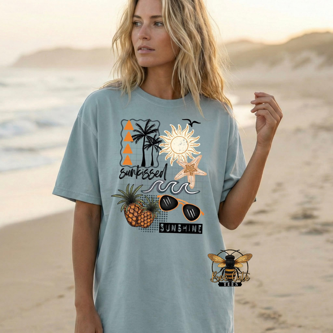 Woman wearing a light blue t-shirt with beach-themed graphics on a sandy beach.