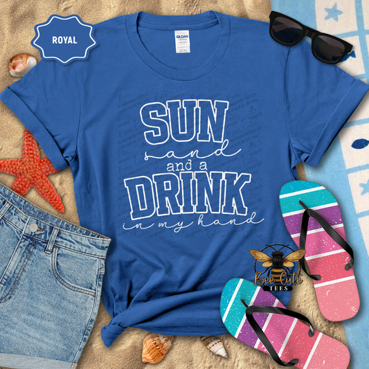 Blue t-shirt with 'Sun and a Drink in my Hand' text, sunglasses, flip-flops, and denim shorts on a beach-themed background.