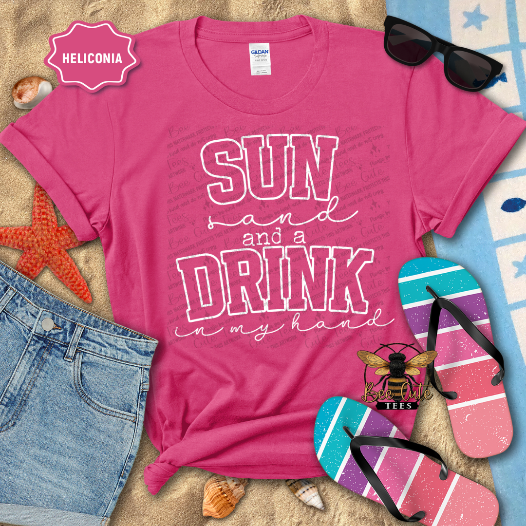 Pink t-shirt with 'Sun and a Drink in my Hand' text, sunglasses, and flip-flops on a beach-themed background.
