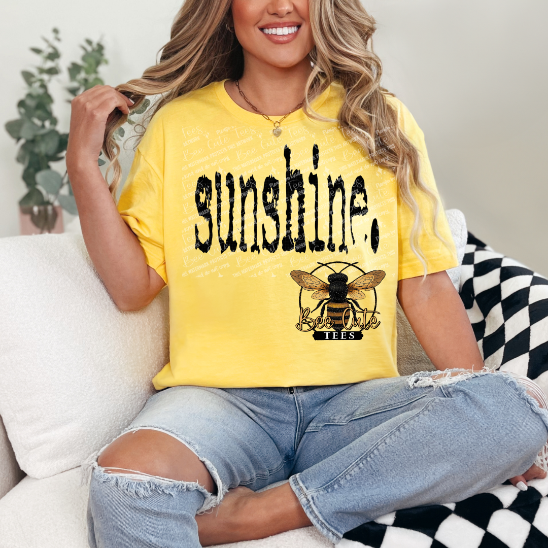 Person wearing a yellow t-shirt with 'sunshine' and a bee logo, sitting on a couch.