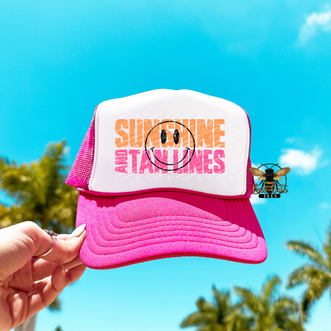 Pink and white cap with 'Sunshine and Tanlines' text against a blue sky background