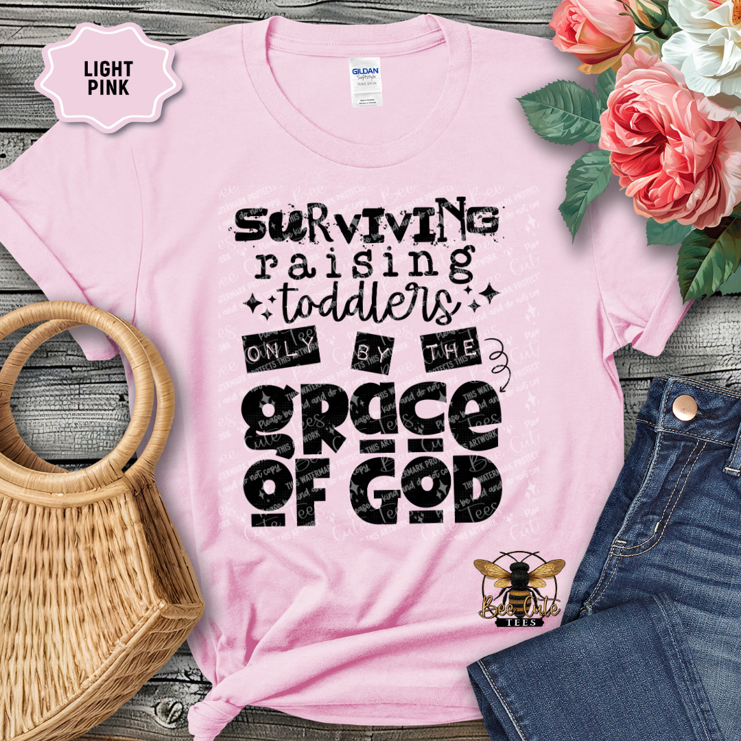 Pink t-shirt with humorous text design on a wooden surface with flowers and accessories.
