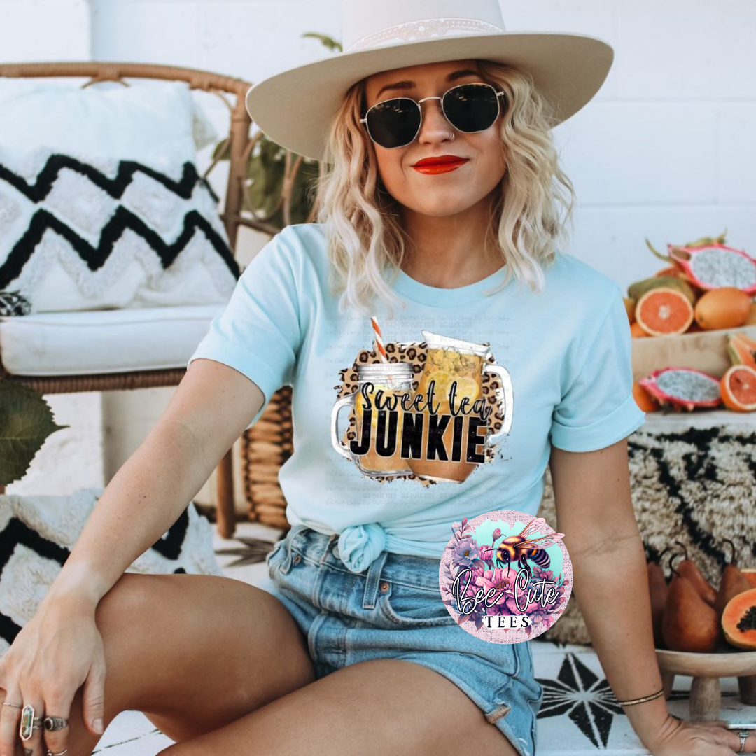 Woman wearing a light blue t-shirt with 'Sweet Tea Junkie' design, sitting outdoors.