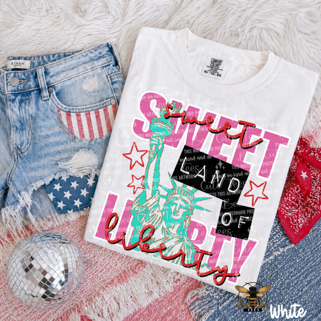 White t-shirt with 'Sweet Land of Liberty' design on a textured surface with denim shorts and disco ball.