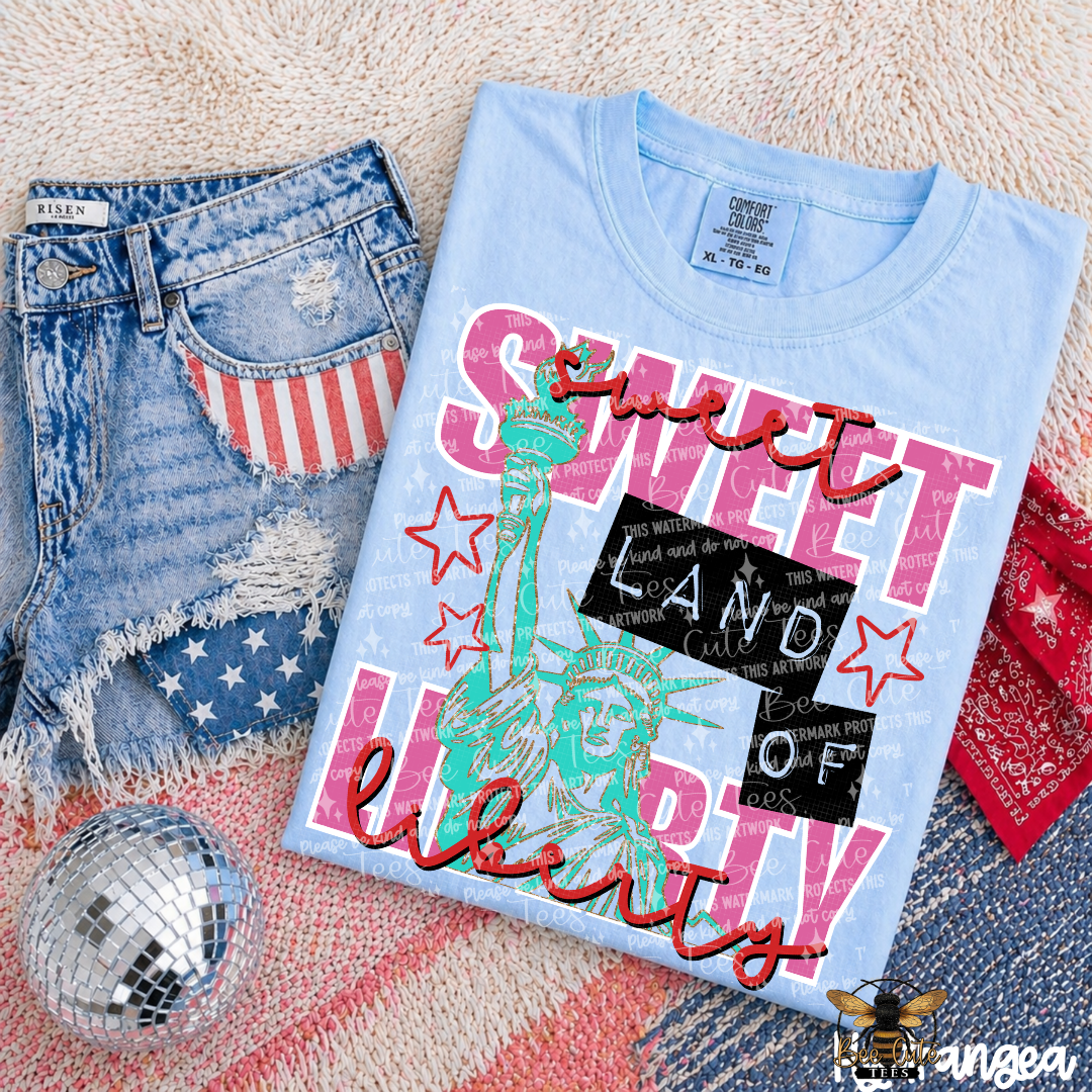 Light blue t-shirt with 'Sweet Land of Liberty' design, distressed jeans, and red bandana on a textured surface.