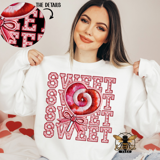Woman wearing a white sweatshirt with a red and pink candy design and 'SWEET' text, holding the sweatshirt with a close-up of the candy design in the corner.