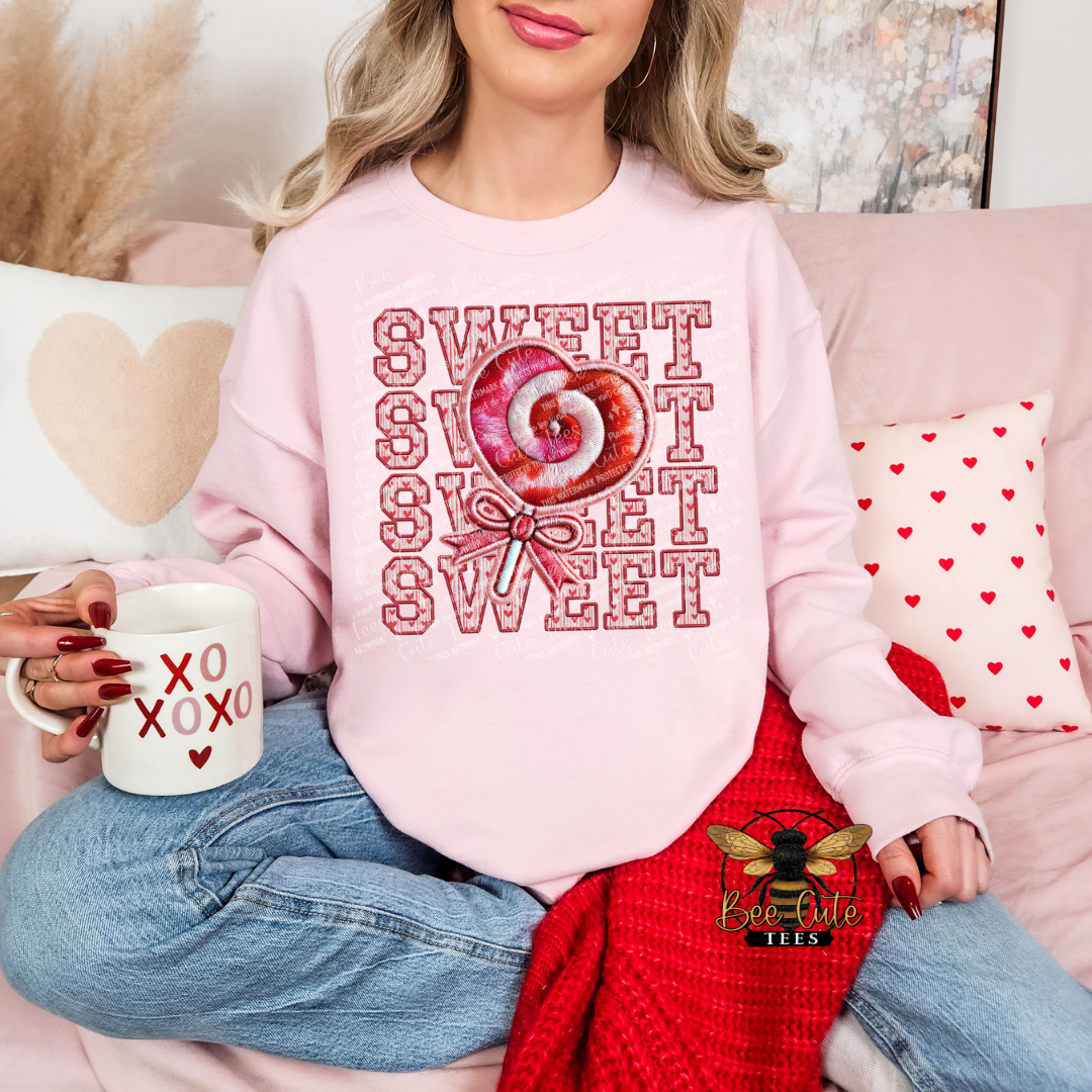 Person wearing a pink sweatshirt with a candy graphic and text, holding a mug with 'XO XOXO' text, sitting on a couch with heart-themed pillows.