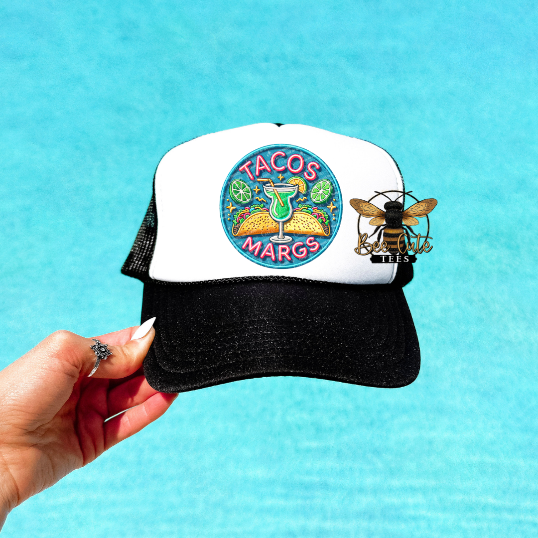 Trucker hat with 'Tacos Margs' design held against a blue background