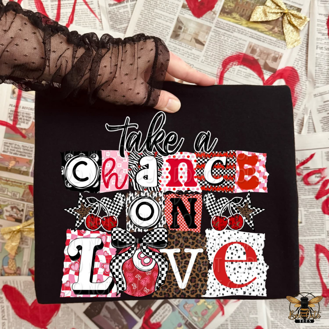 Black shirt with colorful text 'Take a chance on love' held up against a newspaper background.