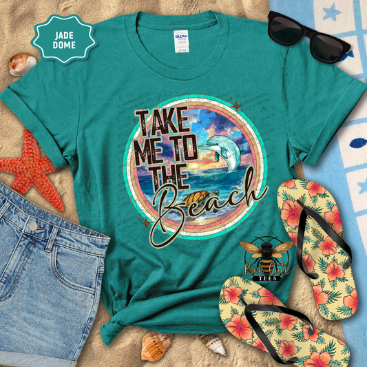 Teal t-shirt with 'Take Me to the Beach' design, sunglasses, flip-flops, and beach accessories on a sandy background.