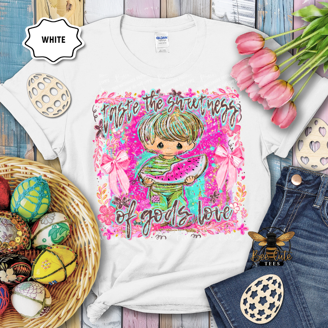White t-shirt with colorful graphic design featuring a child holding watermelon, surrounded by Easter eggs and flowers.