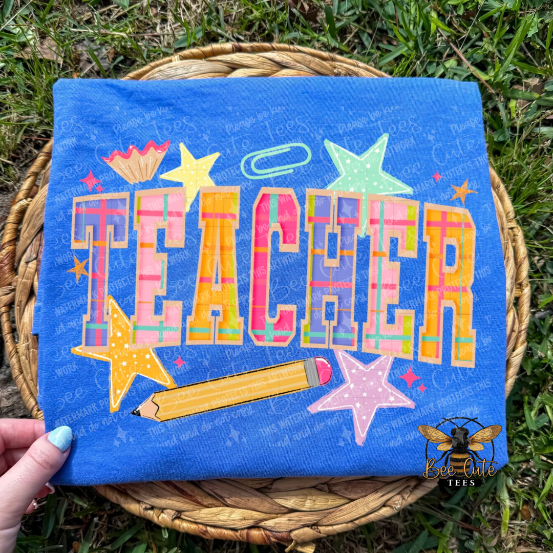 Colorful 'TEACHER' design on a blue background held over grass