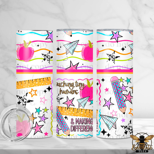 Three insulated tumblers with a colorful school-themed pattern featuring pink apples, stars, pencils, paper airplanes, and the text 'teaching tiny humans & MAKING DIFFERENT' on a white background. A clear lid is shown in the lower left, and a bee watermark is in the lower right.