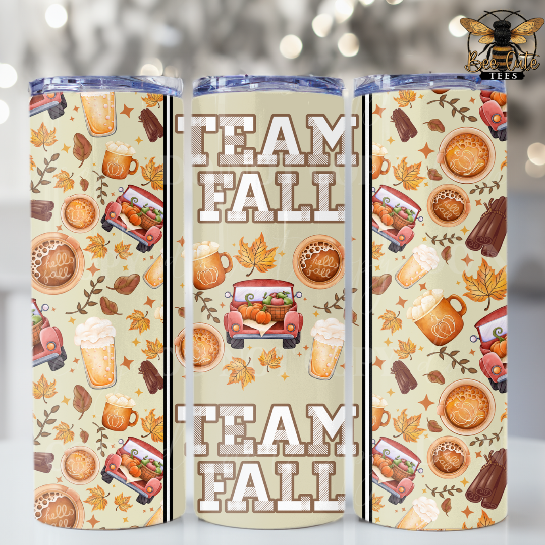 Three insulated tumblers with a fall-themed pattern featuring autumn leaves, coffee cups, hot dogs, and the words 'TEAM FALL' in large letters. The design has a cream background with multicolor illustrations and a blue lid.