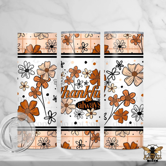 Three insulated tumblers with a floral pattern in orange, beige, and black on a white background, with one tumbler showing the text 'thankful always'. A clear lid is shown in the foreground on a white marble surface.