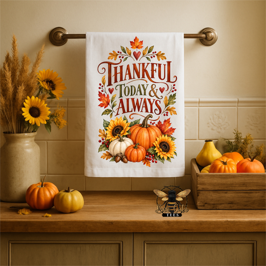 A white kitchen towel with a colorful autumn-themed design hanging on a brass towel bar. The design features the text 'THANKFUL TODAY & ALWAYS' surrounded by pumpkins, sunflowers, and fall leaves.