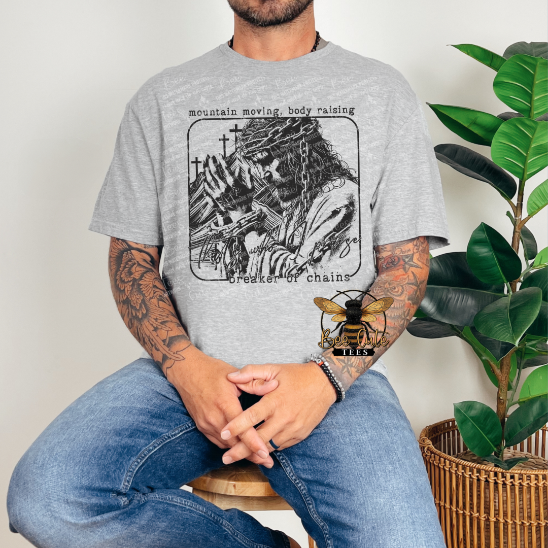 Person wearing a gray t-shirt with a graphic design, sitting in a room with a plant.