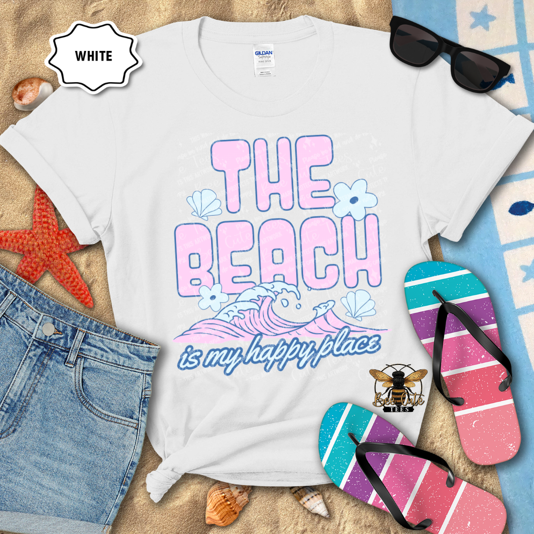 White t-shirt with 'The Beach is my happy place' design on a sandy background with flip-flops and sunglasses.