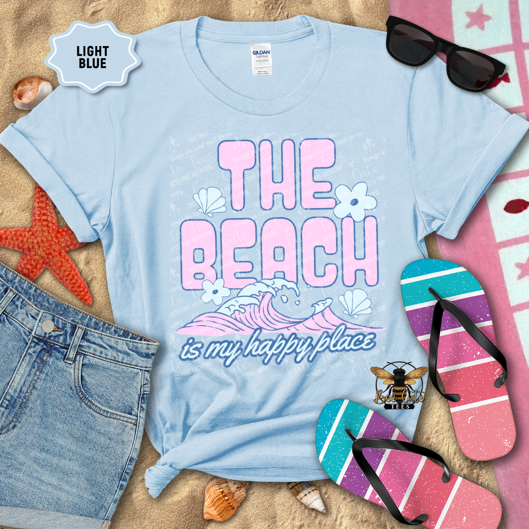 Light blue t-shirt with 'The Beach is my happy place' design on sand with beach accessories.