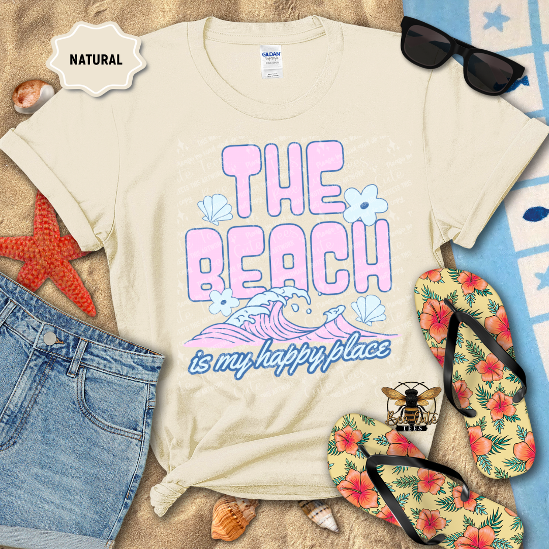 Beach-themed t-shirt with 'The Beach is my happy place' design, sunglasses, flip-flops, and denim shorts on a sandy background.