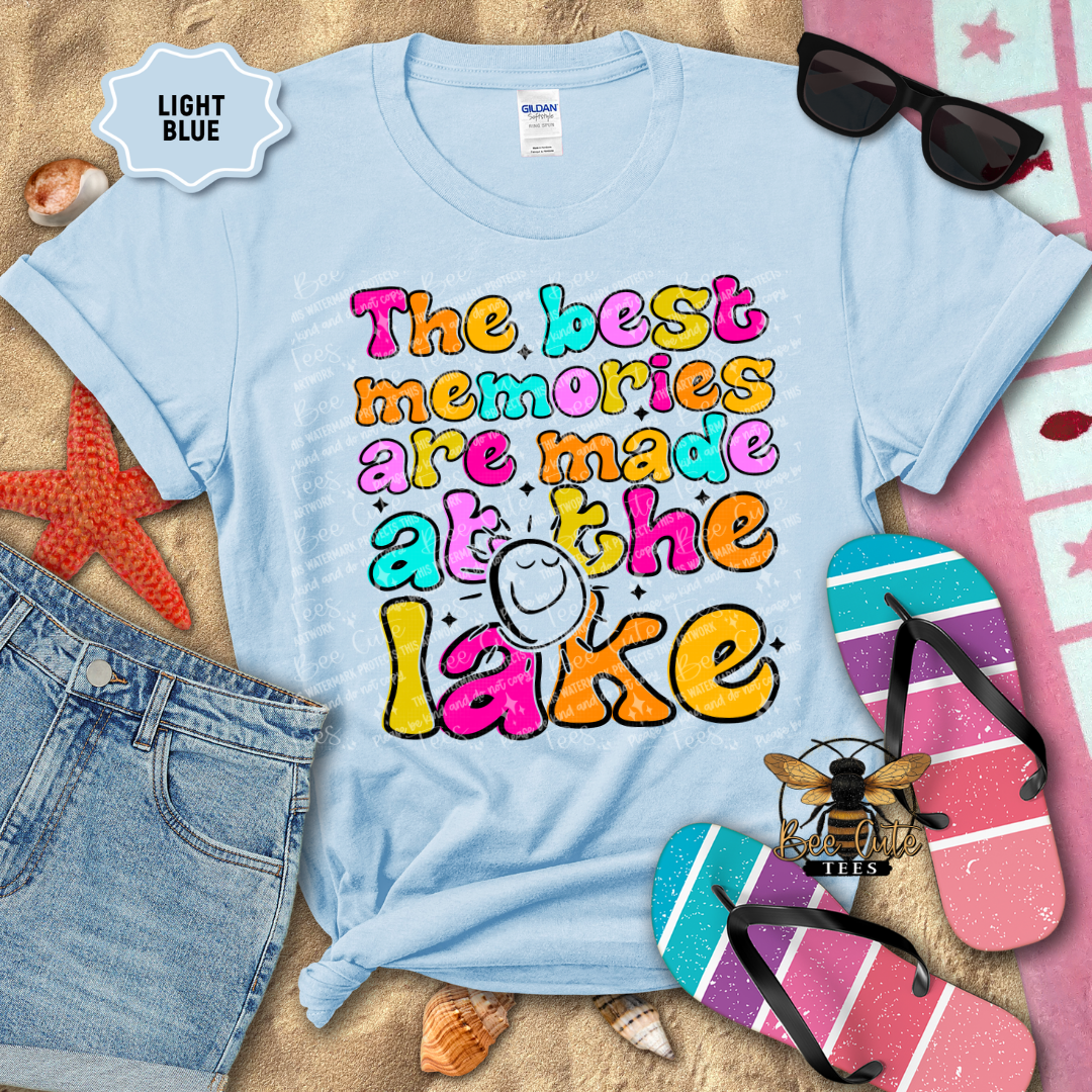 Light blue t-shirt with colorful text 'The best memories are made at the lake' on a beach-themed background.