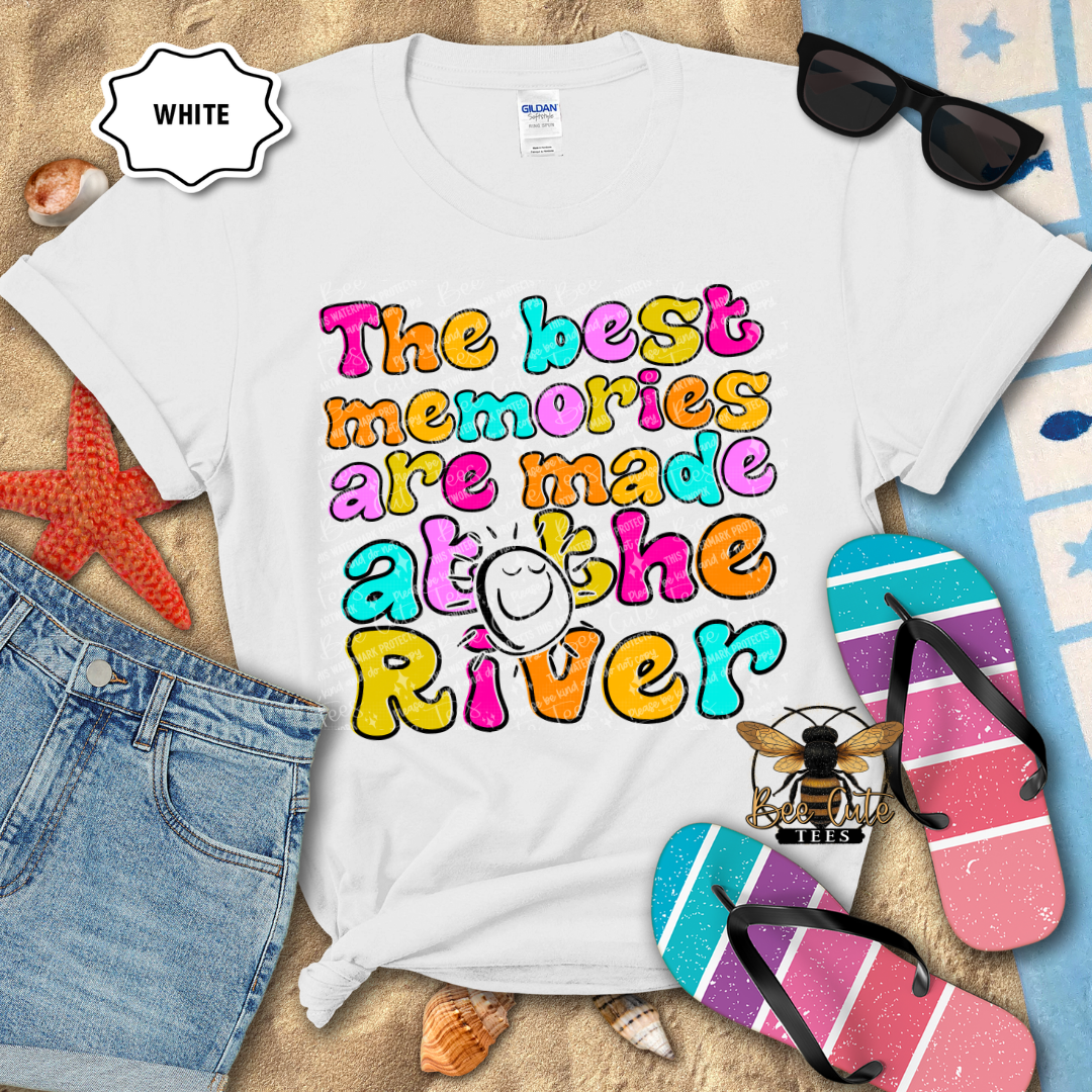 White t-shirt with colorful text 'The best memories are made at the River' on a beach-themed background.