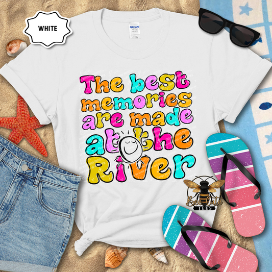 White t-shirt with colorful text 'The best memories are made at the River' on a beach-themed background.