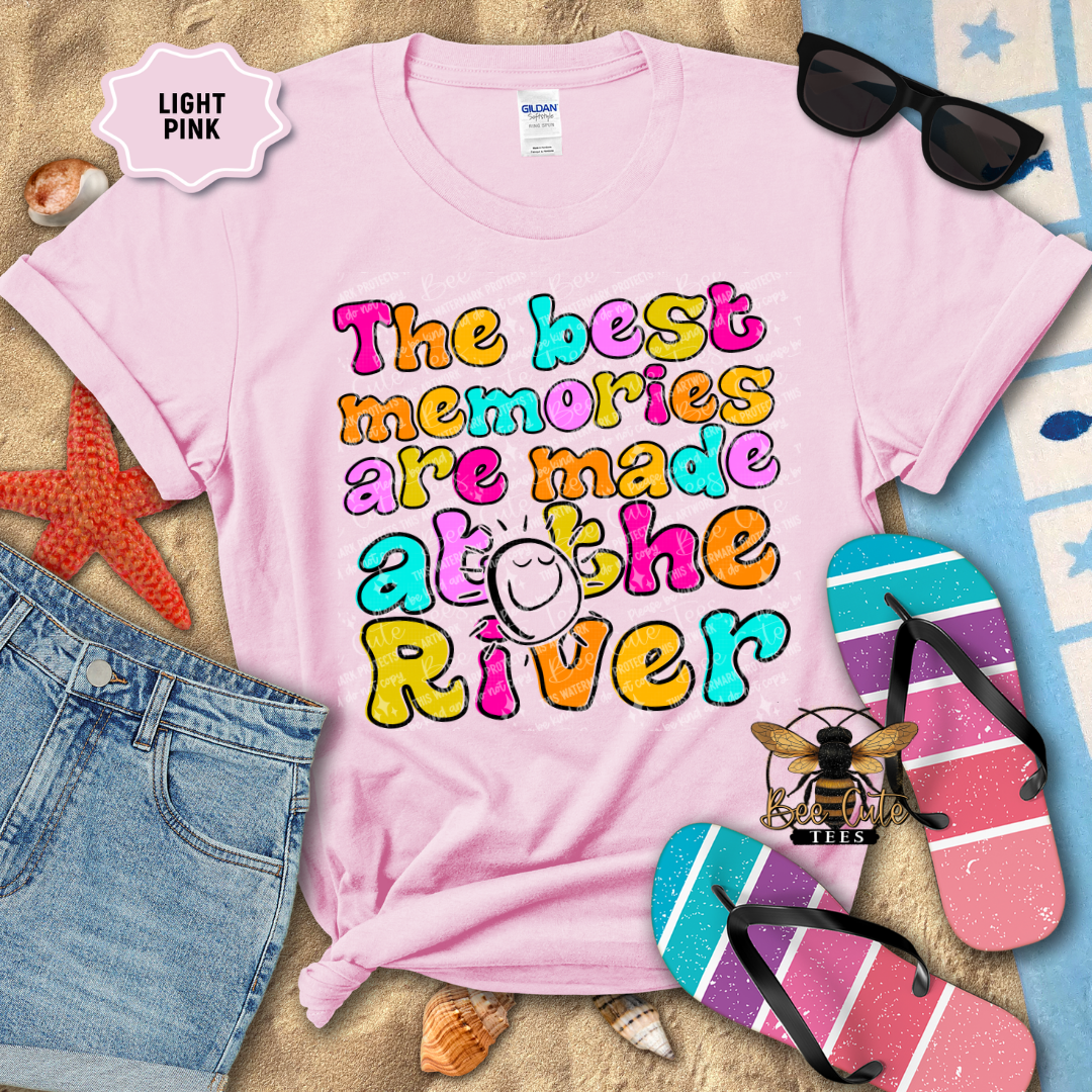 Light pink t-shirt with colorful text 'The best memories are made at the River' on a beach-themed background.