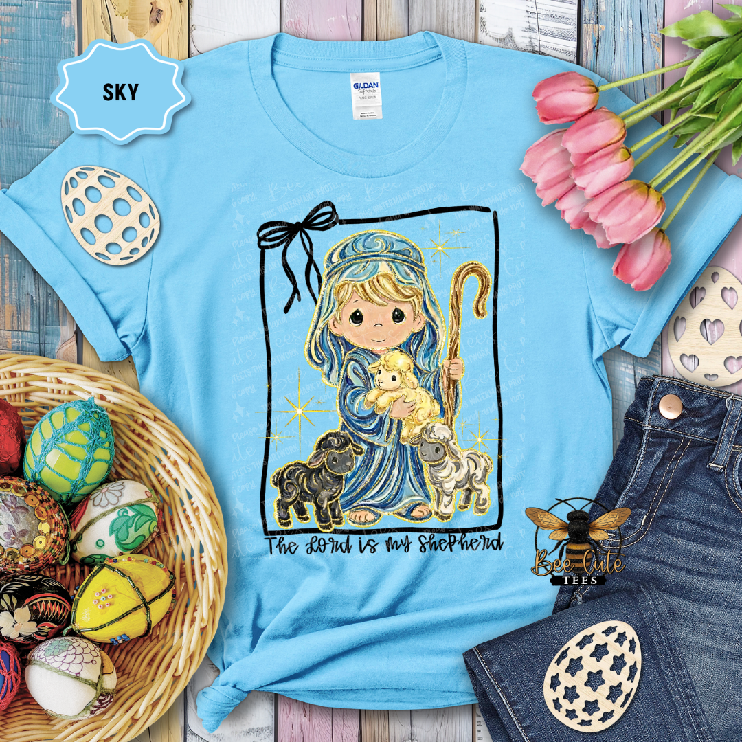 Light blue t-shirt with a religious design featuring a child holding a lamb, surrounded by Easter decorations.