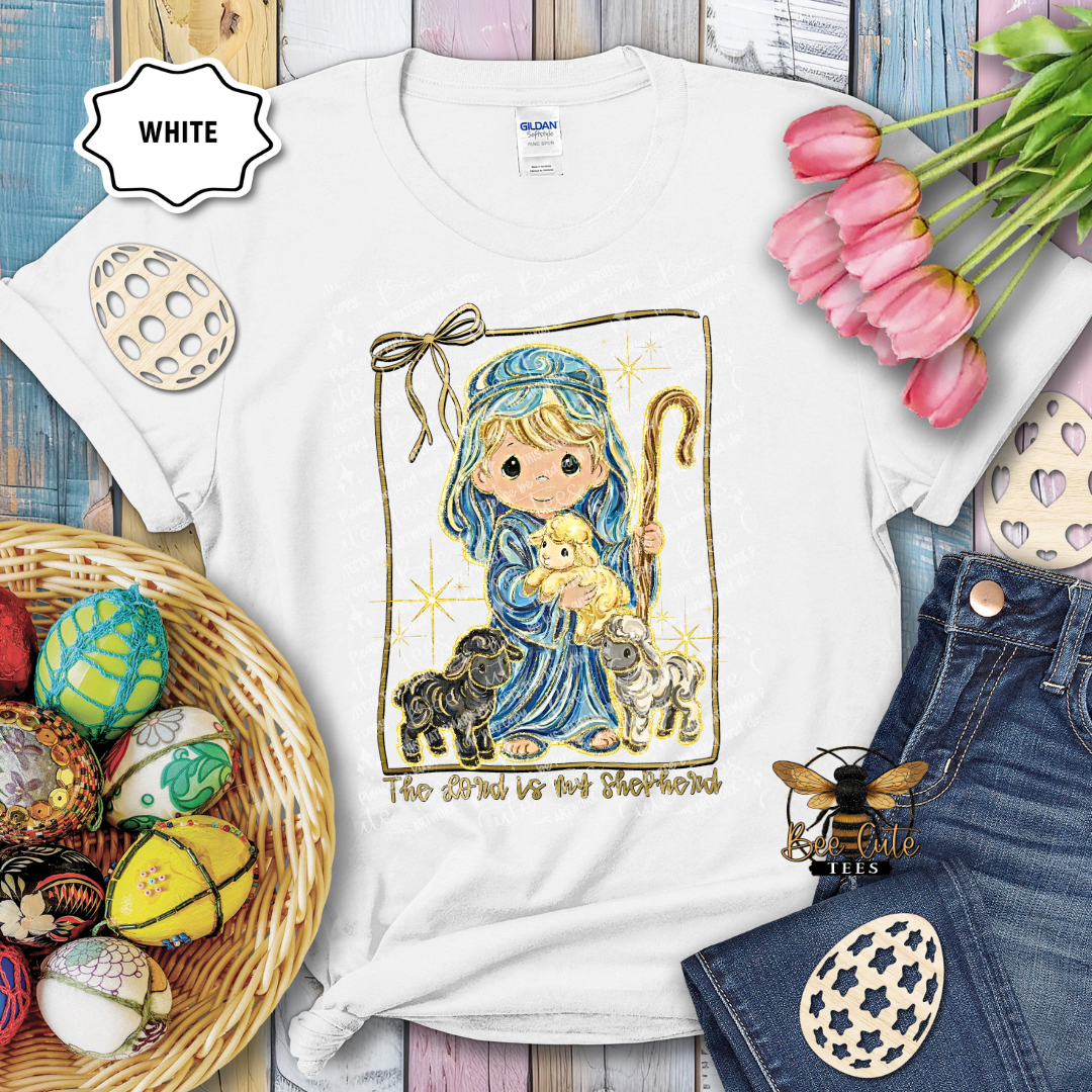 White t-shirt with a religious design featuring a child holding a lamb, surrounded by Easter decorations.