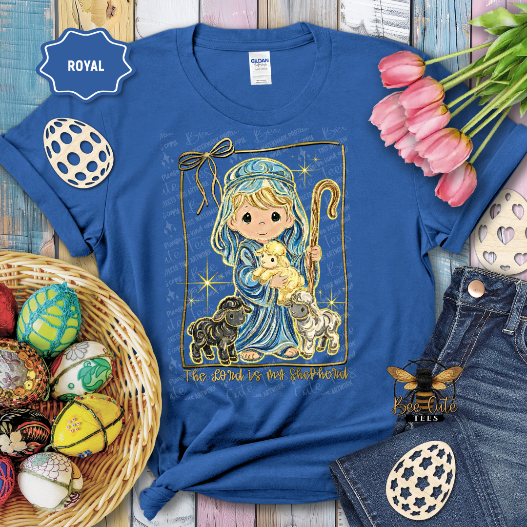 Blue t-shirt with a religious design featuring a child holding a lamb, surrounded by Easter decorations.