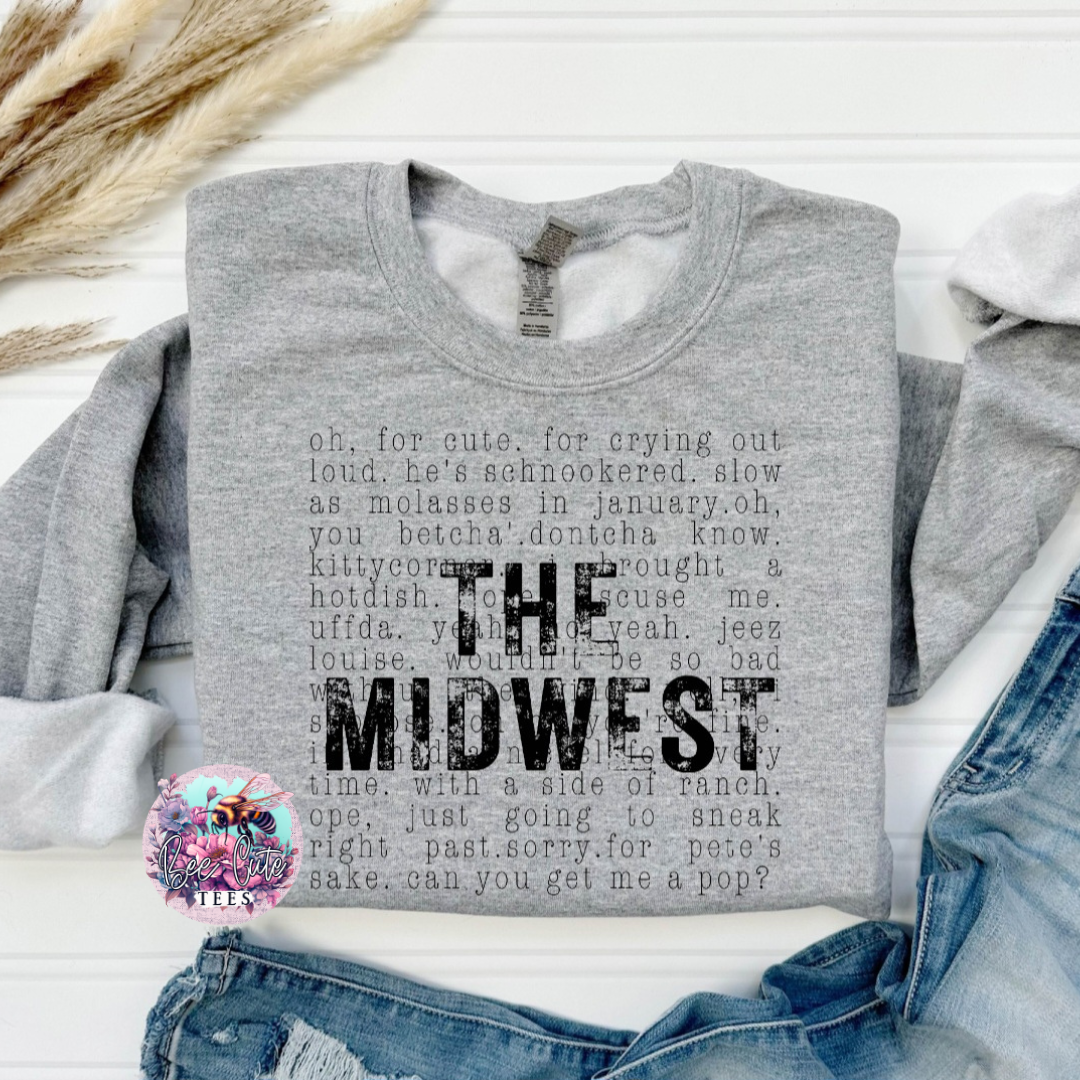 Gray sweatshirt with 'The Midwest' text on a white surface with denim jeans and decorative elements.