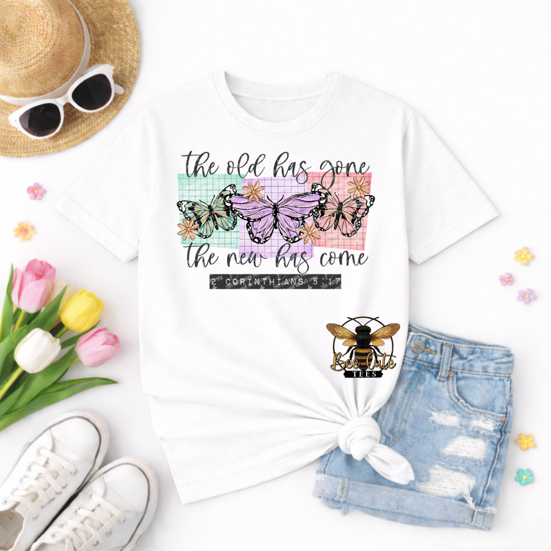 White t-shirt with butterfly design and text, surrounded by sunglasses, tulips, and denim shorts on a white background.