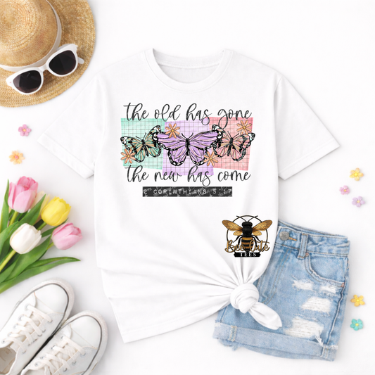 White t-shirt with butterfly design and text, surrounded by sunglasses, tulips, and denim shorts on a white background.