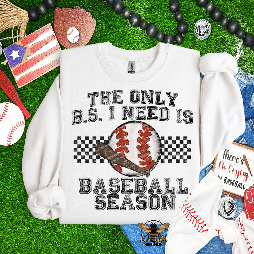 White sweatshirt with 'The Only B.S. I Need is Baseball Season' text on a grass background with baseball-themed accessories.