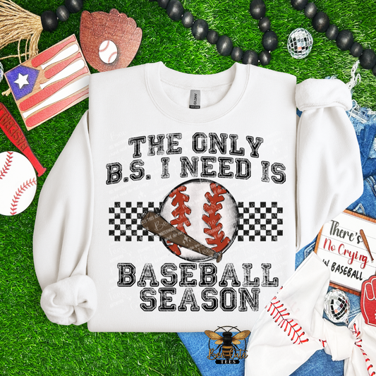 White sweatshirt with 'The Only B.S. I Need is Baseball Season' text on a grass background with baseball-themed accessories.