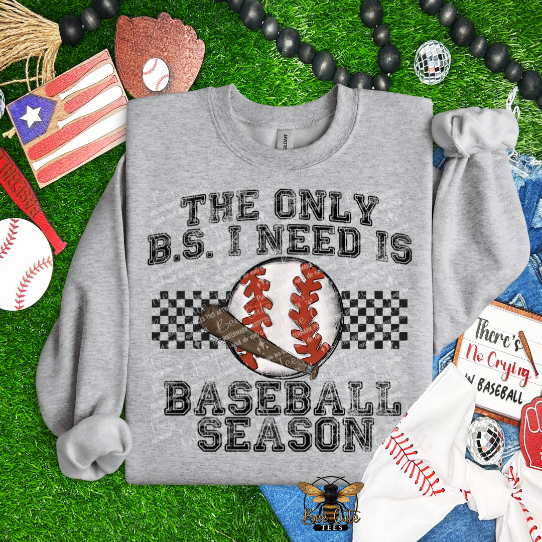 Gray sweatshirt with 'The Only B.S. I Need is Baseball Season' text on a grass background with sports-themed items.