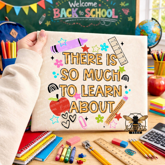 A hand holds a white t-shirt featuring a colorful 'Back to School' quote. The scene is a busy, well-lit desk filled with school supplies like notebooks, pencils, a globe, and a chalkboard in the background.