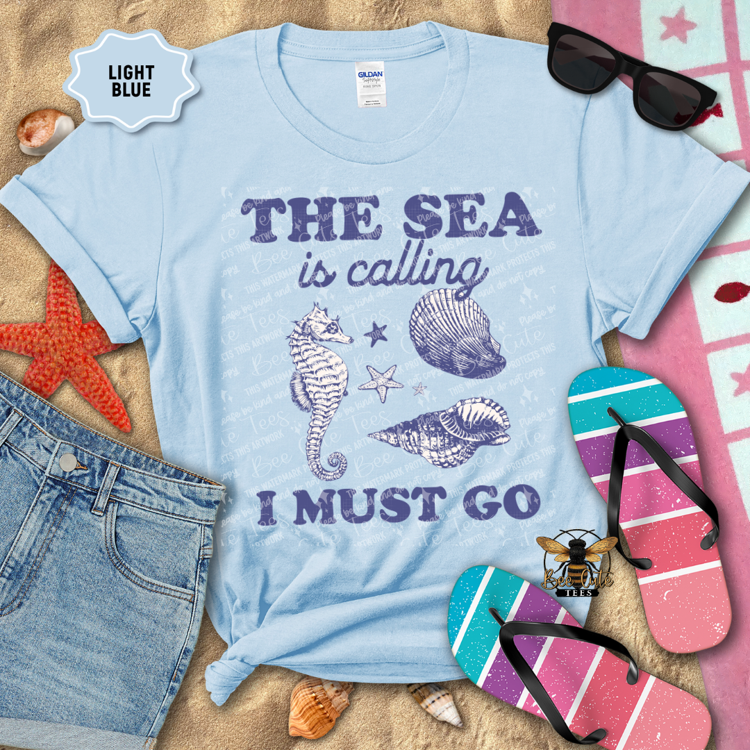 Light blue t-shirt with beach-themed design and accessories on a sandy background