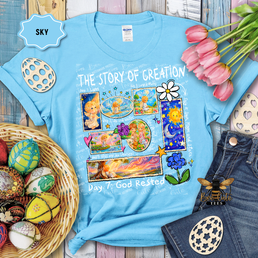 Blue t-shirt with 'The Story of Creation' design, surrounded by Easter decorations on a wooden surface.