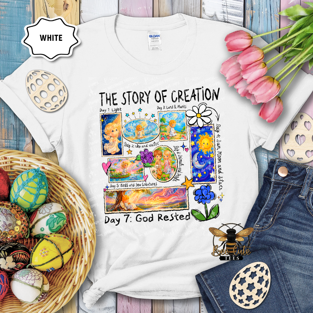 White t-shirt with 'The Story of Creation' design, surrounded by Easter eggs and flowers on a wooden surface.