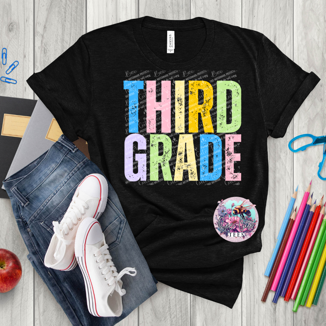 Black t-shirt with 'THIRD GRADE' in colorful letters on a wooden surface with jeans, sneakers, and school supplies.