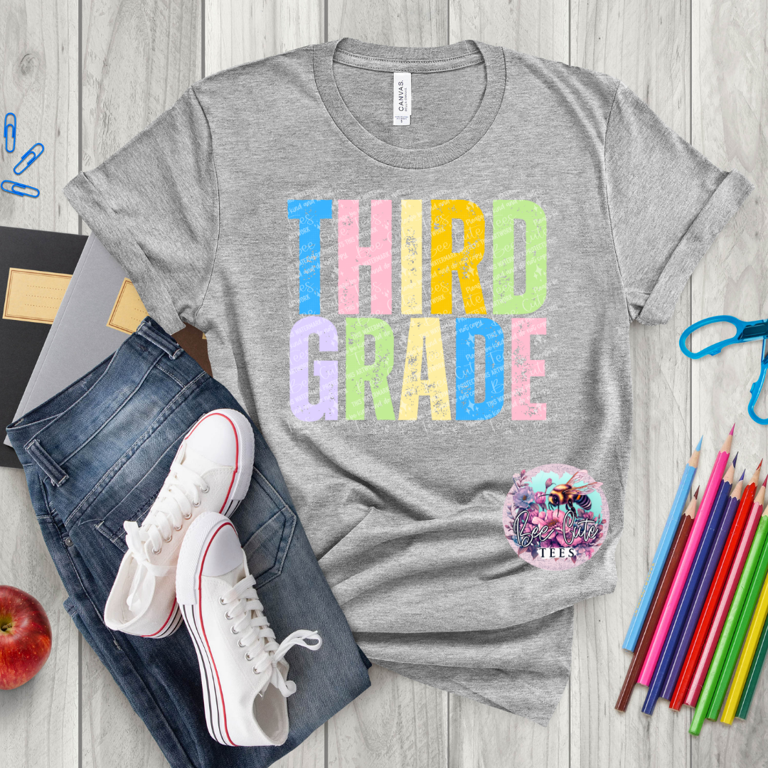 Gray t-shirt with 'THIRD GRADE' text, jeans, sneakers, and school supplies on a wooden surface